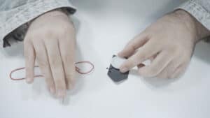 Close-up of a person holding a paradox button with a string on a white surface.