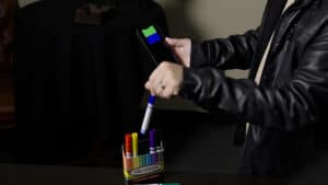 Person matching colored pens to a smartphone screen for magic trick demonstration.