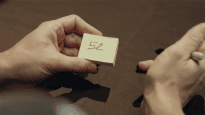 Close-up of a person holding a sticky note with the number 52 for magic tricks.