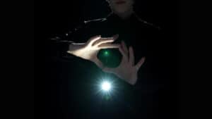 Performer holding glowing orb with light effects, showcasing magic tricks.