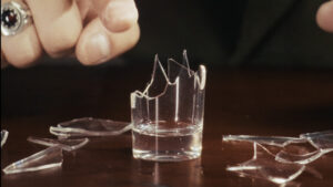 Close-up of shattered glass pieces on a dark surface, magic trick demonstration.
