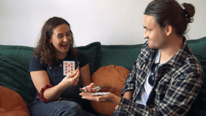 Magician performing a card trick with a woman on a sofa, showcasing magic skills.