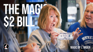 Woman performing magic with a $2 bill in a magic shop setting.