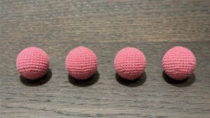 Four light pink crocheted balls arranged on a wooden surface for magic tricks.