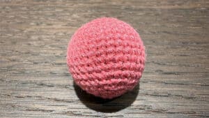 Light pink crochet ball used in magic tricks, shiny and textured for illusions.
