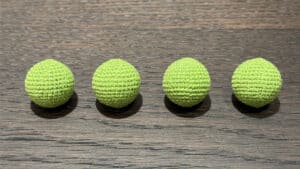Four grass green crochet balls on wooden surface, magic trick props.