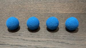 Four royal blue crochet balls on wooden surface, magic trick props.