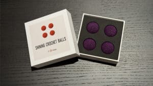 Four dark purple crochet balls in a display box for magic tricks.