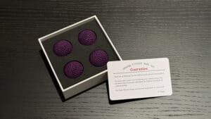 Four dark purple crochet balls in a box for magic tricks and illusions.