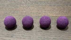 Four dark purple crochet balls arranged on a wooden surface for magic tricks.