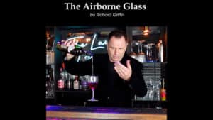 Magician performing a wine levitation trick with a glass in a bar setting.