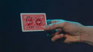 Playing card with intricate back design, held between fingers against a dark background.