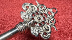 Silver ornate key with cloud and swirl designs on a red background.