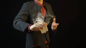 Performer demonstrating a card trick with smoke at a magic show.
