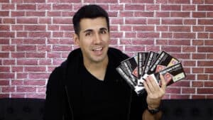 Magician demonstrating paper-to-money illusion with playing cards in front of brick wall.