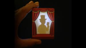 Shadow puppet of a magician with a top hat behind a curtain.