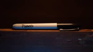 Close-up of a white marker labeled "Pigmento" on a dark wooden surface.