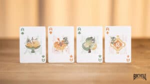Four Ace playing cards featuring a bicycle mascot in different colors on a wooden surface.