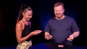 Magician performing a card trick with a woman on stage.