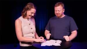 Two magicians performing a card trick on stage with playing cards.
