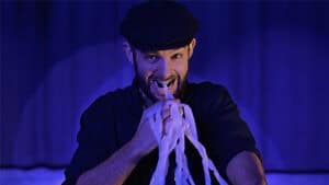 Performer demonstrating the Mouth Coil Pro magic trick with a coil of paper in hand.
