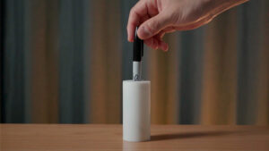Hand inserting a Sharpie into a white container for a magic trick demonstration.