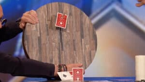 Up of Cyril performing card magic with a wooden table and red playing cards.