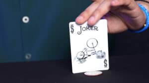 Close-up of a magician performing a card trick with a Joker card and coin.