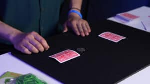 Close-up of a magician performing a card trick with two cards and a coin on a black table.