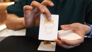 Close-up of a person performing a magical hamster card trick with a small hamster illustration.