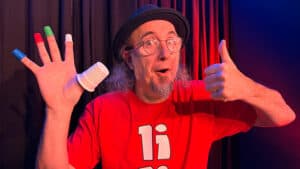 Magician performing a thimble magic trick with colorful cups and hand gestures.