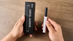 Hand holding a white and black marker pen with packaging on a wooden surface.