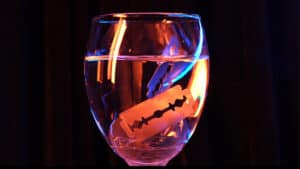 Glass of water with floating paper scroll and bat silhouette, eerie lighting.