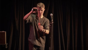 Young magician performing a drink trick on stage with a microphone in the background.
