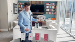 A magician performs Jumbo McDonald Aces with red-backed cards in a modern living room.