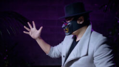 Performer in mask and hat performing stage magic with dramatic lighting.