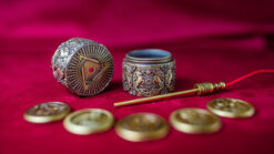 Silver box and coins for magic tricks on red fabric background.