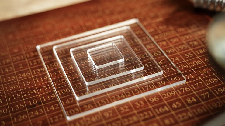 Close-up of transparent acrylic blocks arranged on a wooden number grid for a magic square trick.