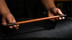 Folding wand magic trick with wooden wand and black tips, performed on a dark surface.