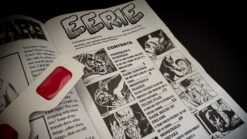 Close-up of a comic book page with eerie illustrations and a red magic prop for stage tricks.