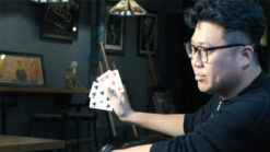 Performer displaying a magic bill trick with playing cards in a dimly lit room.