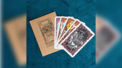 Close-up of a tarot card deck with illustrated cards and a brown envelope on a blue surface.