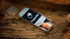 Small orange magic capsule inside a silver case on wooden surface.