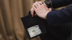 Close-up of a hand holding a wallet with a watch and a ring, demonstrating a magic trick.