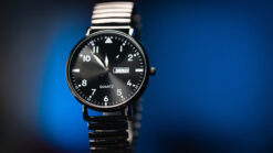 Close-up of a black wristwatch with a black band and white dial, showcasing a magic trick effect.